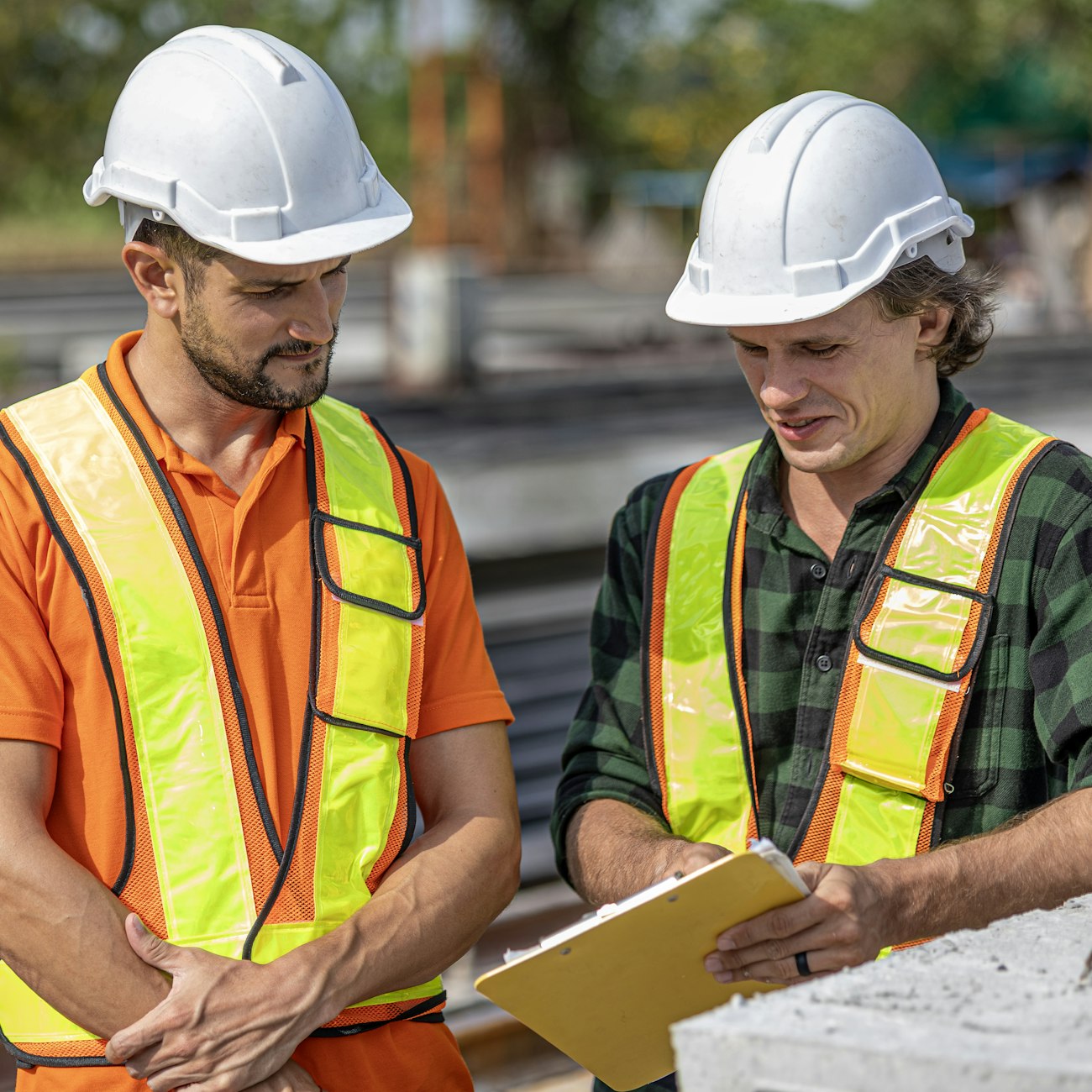 Two construction professionals in hard hats reviewing a clipboard beside precast concrete elements